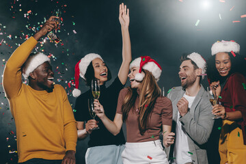 People in Christmas hats dancing and throwing confetti while celebrating New Year in night club
