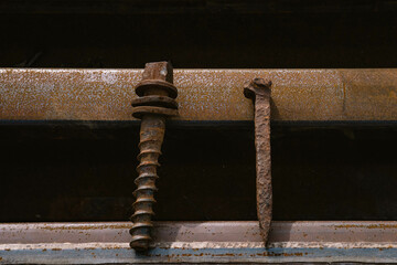 One very old rusty railroad spike and one rusty screw spike lay on two old rusty rails, close up...