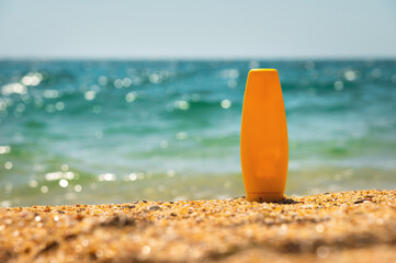 empty cosmetic skin care cream or sunscreen on sandy beach on sea background. a yellow bottle of cream stands on the sand. Blank template for brand presentation