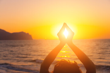 young woman raises her hands, praying in the light of sunset or sunrise. silhouette of female hands during sunset