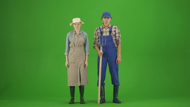Portrait of couple in casual and rubber boots on chroma key green screen. Woman and man gardeners standing with pitchfork looking at camera.