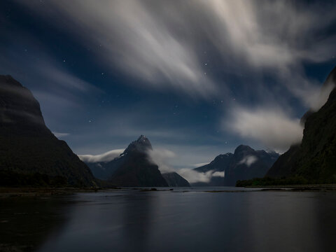 Moonlit night sky and clouds over Mitre Peak on the shore of Milford sound; South Island, New Zealand