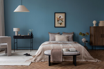Warm and cozy bedroom with mock up poster frame, cozy bed, beige bedding, blue wall, pillows, wooden sideboard, bench, gray armchair, vase with flowers and personal accessories. Home decor. Template.