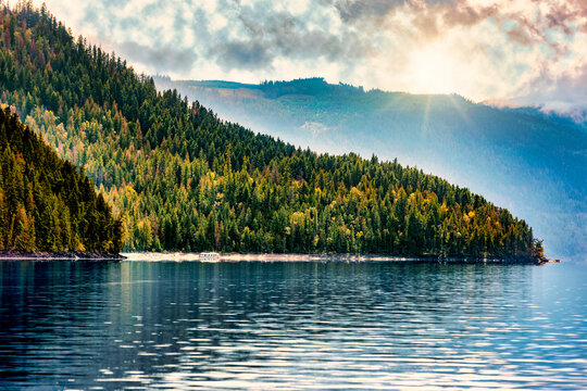 Houseboat parked on Shuswap Lake in autumn with sunrays over the mountains, British Columbia, Canada