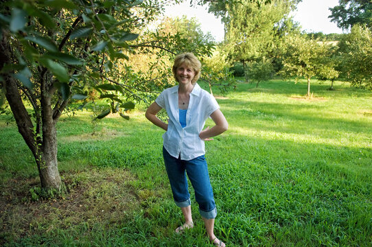 Woman stands posing in the shade of a tree in an orchard; Greenleaf, Kansas, United States of America
