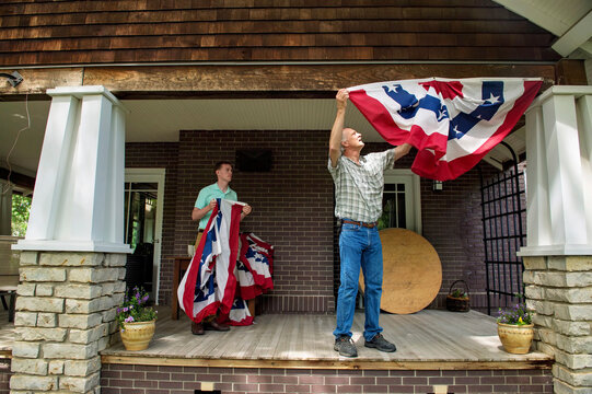 Two men hang up patriotic banners on the porch of a house; Lincoln, Nebraska, United States of America
