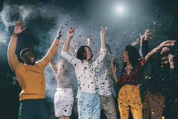 Group of young joyful people dancing and throwing confetti while having fun in night club together