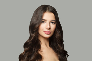 Fototapeta premium Beautiful brunette model woman with long wavy hair and shiny fresh skin posing on white background, fashion beauty studio portrait