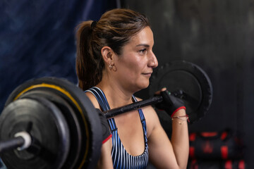 Fototapeta na wymiar Mexican latina adult female holding a barbell at face level in a gymnasium