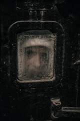 A girl's face behind a dirty window in an abandoned bunker. A shabby rusty door. Dirty glass.
