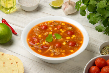 
Easy Mexican chicken and rice soup in a white soup bowl on a rustic white table with ingredients.
- 686758948