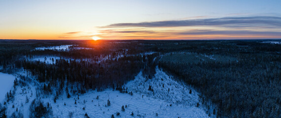 Winter cold red Sunset - the Sun hides behind the horizon line, snowy forest landscape of Northern Scandinavian landscape in Lapland, Sweden. Aerial photo panorama - obrazy, fototapety, plakaty