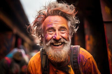 Joyful elderly man with a bright, paint-covered face laughing during a vibrant Holi festival celebration outdoors.