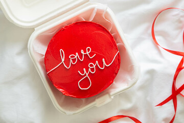Red bento cake in Korean style with I love you inscription on a white blanket in bed, top view, Valentine's Day celebration concept.