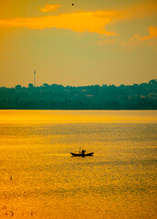 A man fishing in a small boat on Lake Victoria, Uganda at sunrise.