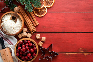 Christmas culinary background with ingredients for cooking christmas baking cranberries, sugar, cinnamon and Christmas tree branches on rustic old red wooden table background.Top view copy space.