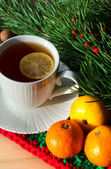 Tangerines and a cup of morning tea with lemon against the background of green branches of a Christmas tree. Decorations for the New Year and Christmas.