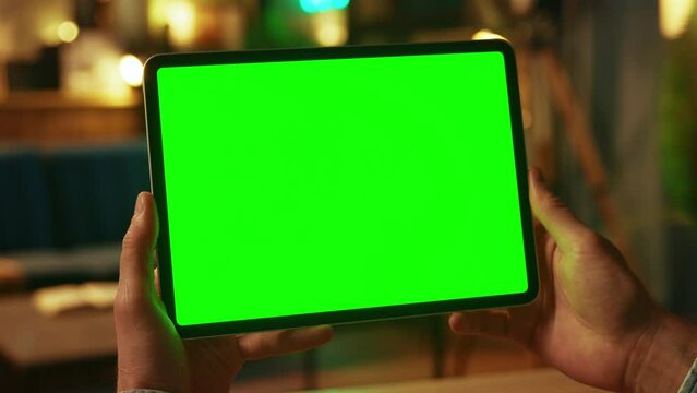 Close up hands man holding tapping on tablet computer with horizontal green screen. Mock up. Dark room