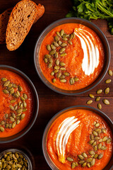 Pumpkin soup with seeds, sour cream, spices and bread in dark masks on a wooden table, shot close-up from above. The concept of healthy vegetable soups. Concept of healthy eating or vegetarian food