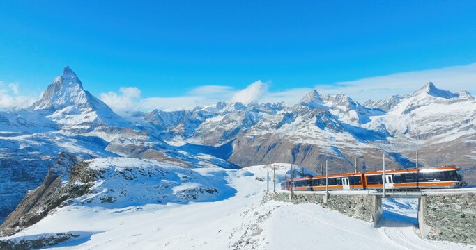 Panoramic landscape of Gornergrat bahn railway climibing up the summit station with Matterhorn mountain peak background in Zermatt on a sunny winter day. Swiss Alps, Switzerland travel journey trip.