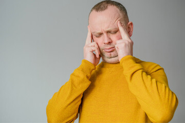 Portrait of a young man suffering from headacthe, touching his temples, closed his eyes on a gray...