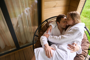 Pretty female and handsome man embracing while sitting on porch