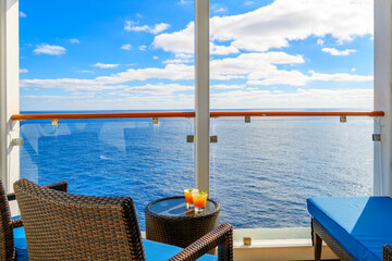 Two tropical mixed alcohol drinks sit on a small end table on the balcony veranda of a cruise ship stateroom on a sunny day on the Mediterranean Sea. - obrazy, fototapety, plakaty
