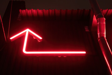 Red arrow indicated directions on the facade of a building with a metal pipe at night. The arrow...