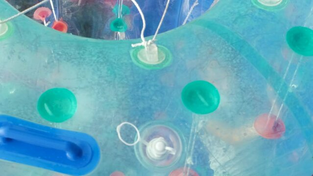 Vertical video. Young girl playing inside water roller at amusement park. Child having fun in zorb cylinder on the water in an inflatable pool