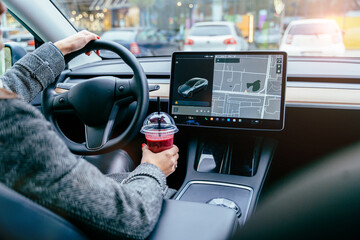 Rear view of unrecognizable female driving modern electric car. Tesla tablet screen.