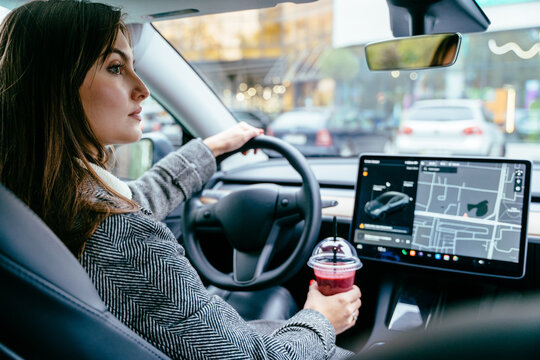 Success businesswoman traveling by car with coffee to go. Woman driving and holding a smoothie drink cup. The concept dangerous driving.
