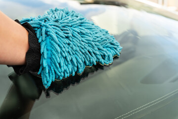 Car wash and self-service concept. A man washes the car windshield with a large blue washcloth.