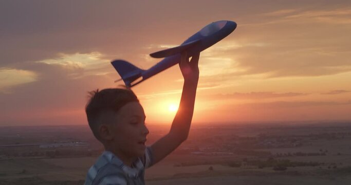 Portrait of happy boy running with toy plane against stunning sunset backdrop. Happy kid at sunset. Silhouette shot