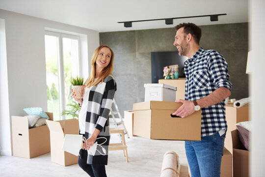 Happy couple moving house carrying cardboard box and plant