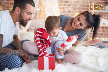 Boy opening Christmas present with his parents in bed