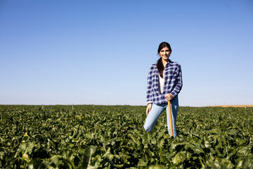 Young woman farmer with hoe on field