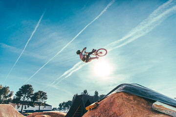 Carefree young man performing stunt with bicycle against blue sky at park during sunset