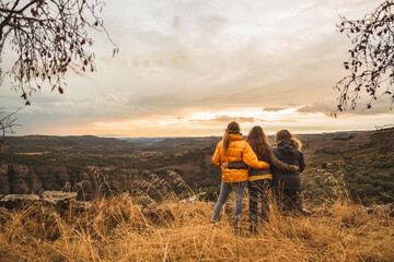 Spain, Alquezar, three friends embracing on a hill overlooking the scenery