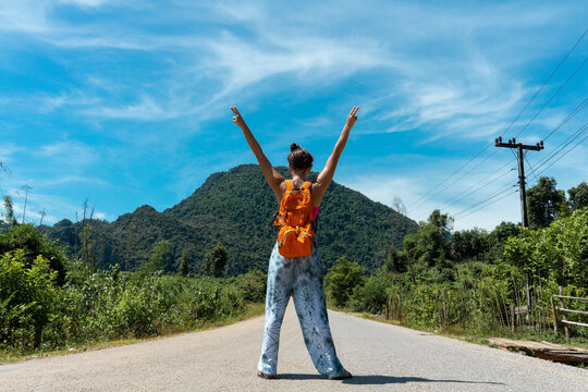 Laos, Vang Vieng, woman standing on country road with raised arms
