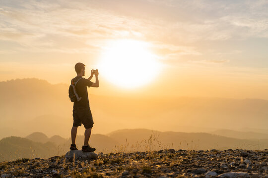 Spain, Barcelona, Natural Park of Sant Llorenc, man hiking and taking a picture of the view at sunset