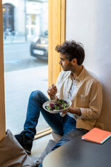 Man eating a salad sitting at the window in a restaurant looking out