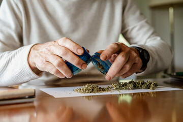 Midsection of elderly man removing weed from grinder on paper at home