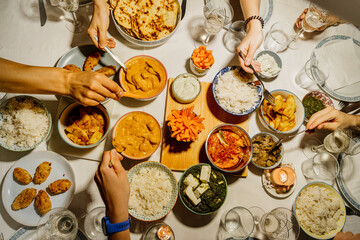 Hands of people dining together around table set with Indian food