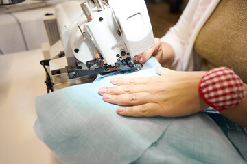 Dressmaker works on a sewing machine with blue fabric