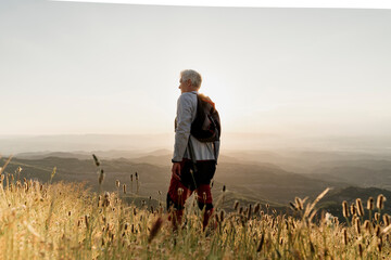 Active senior male hiker standing on mountain while looking at landscape during sunset