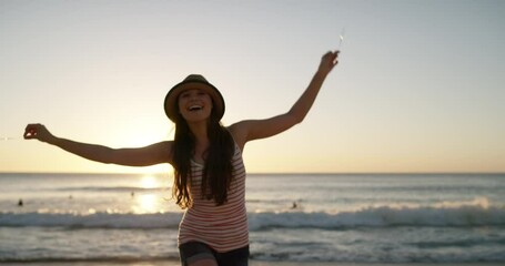 Woman, joy and beach with fireworks, dance and enjoy the ocean, nature and seaside. Travel, holiday and smile for vacation, calm and peace with freedom, lens flare and outdoor to relax, hat and play