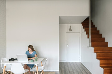 Woman sitting at table working on graphics tablet and laptop