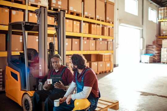 Two Warehouse Workers on Break with Coffee and Forklift in Background