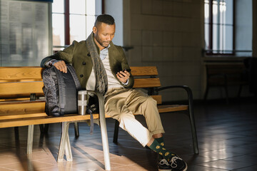 Stylish man using smartphone while sitting on a bench in a train station