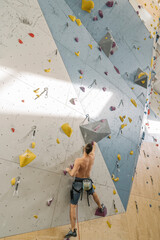 Shirtless man climbing on the wall in climbing gym